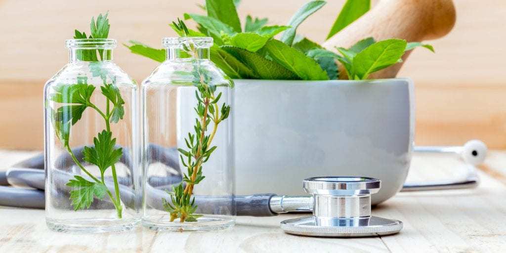 Herbs in glass bottles next to a doctors stethoscope to represent natural alternatives to traditional healthcare. 