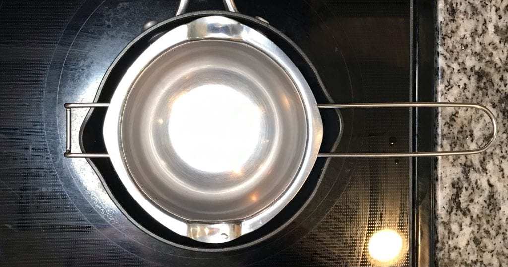 Double boiler sitting on saucepan on stove in preparation for a DIY mica tinted lip balm recipe.
