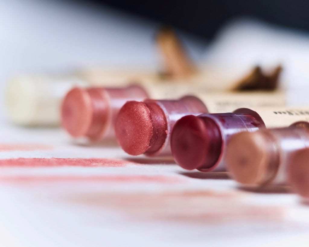 Six different shades of handmade and organic tinted lip balm with mica, ranging from light pink to dark brown.