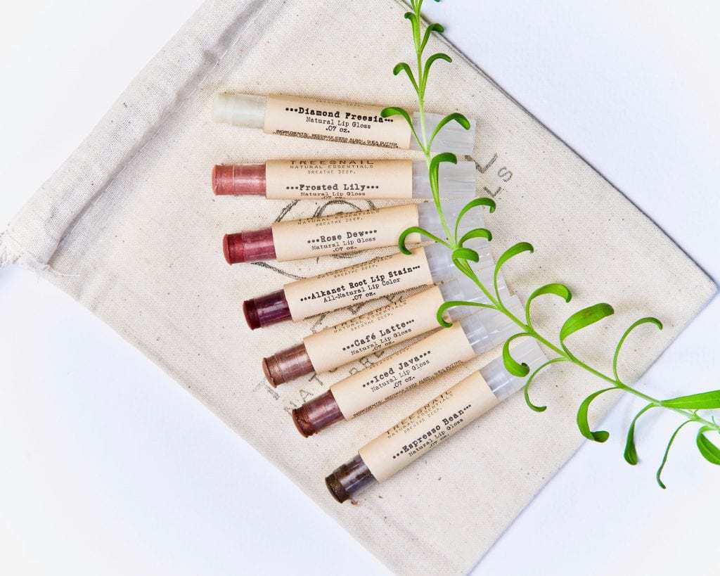 7 organic mica tinted lip balms in a muslin bag, ranging from clear shimmer to dark brown.