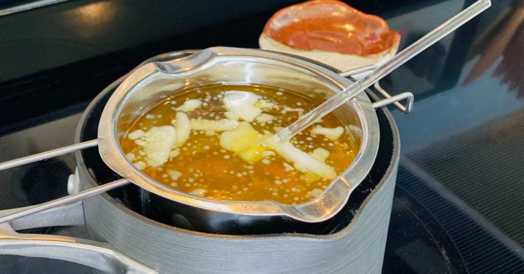 Stirring melted ingredients for organic belly balm with a glass rod.