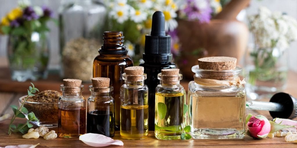 Carrier oils, herbs, and essential oils displayed together on a table in clear bottles with corks.