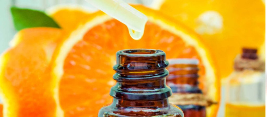orange essential oil being dropped into an amber glass bottle